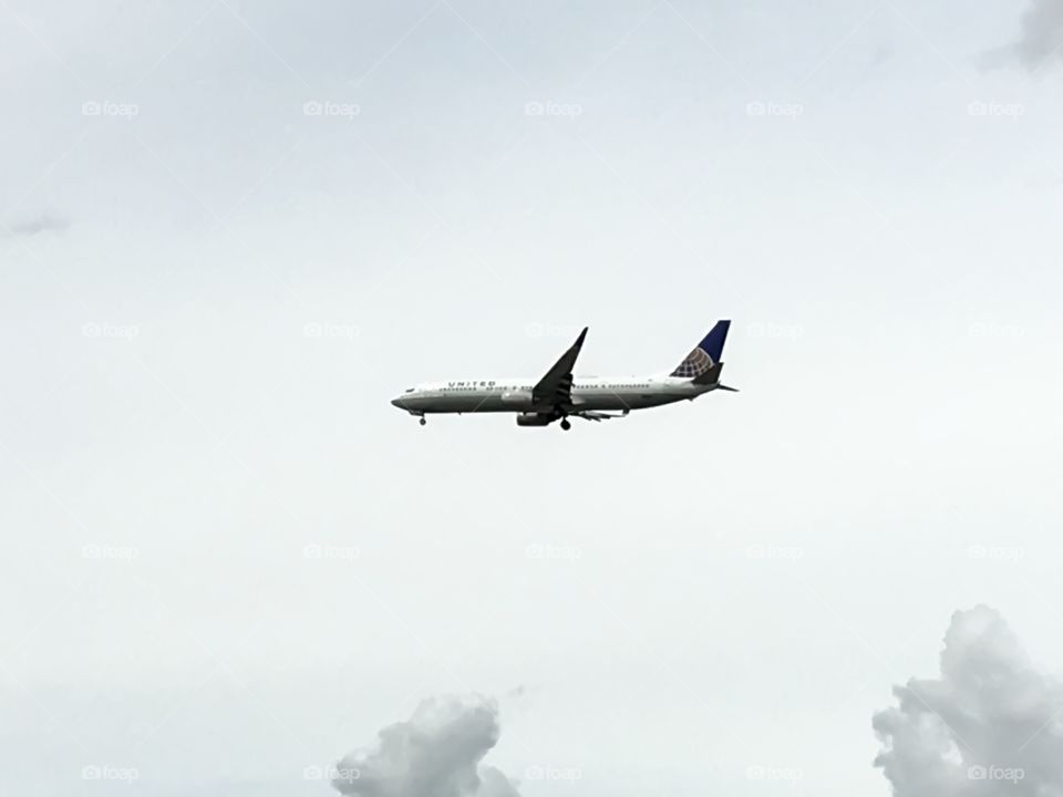 Commercial Airplane jet flying low in overcast sky with wheels down landing gear in preparation for landing 