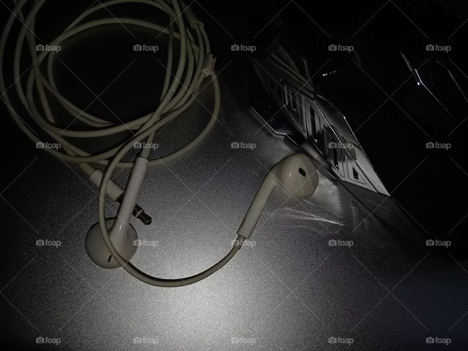 white ear plugs with black gaming mouse above silver laptop closeup in darkness