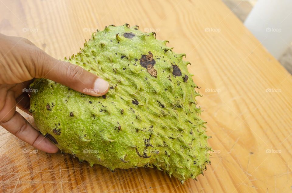 Holding A Soursop Against A Board Surface