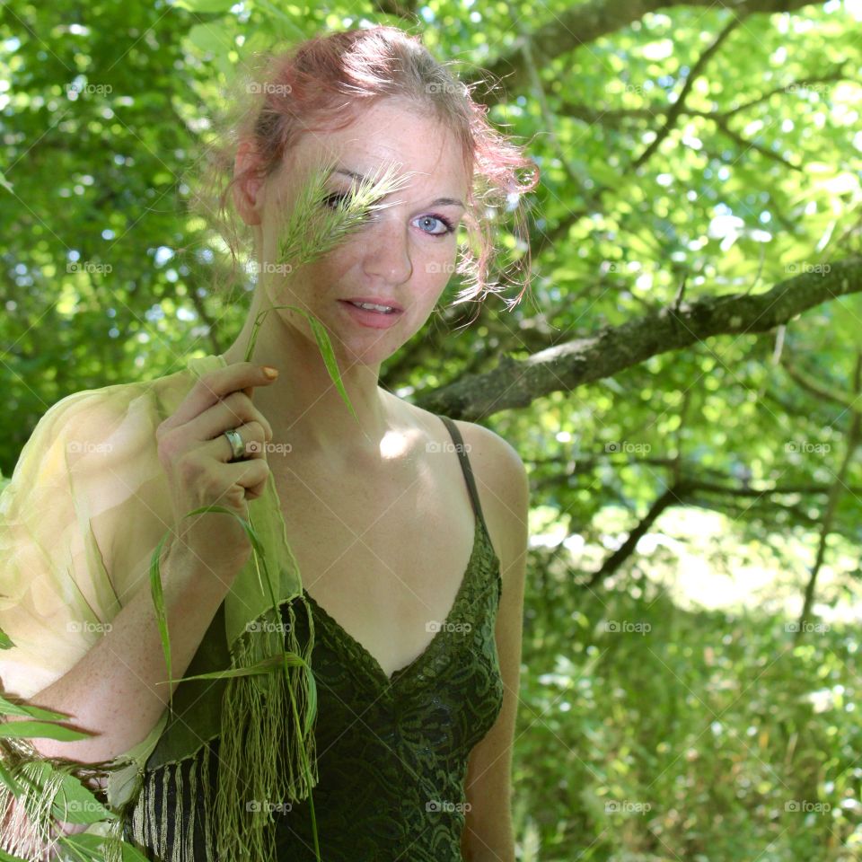 Never judge yourself through the eyes of someone else. Pretty woman peeking through green foliage.