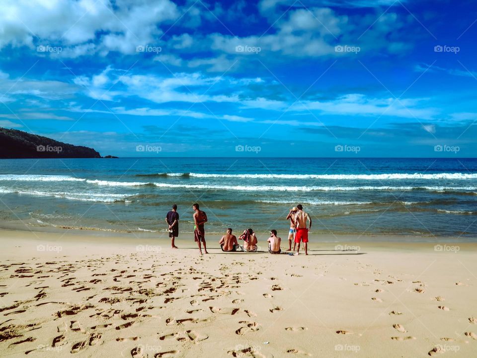 Beautiful shot of the Sunrise on the Atlantic ocean, in Praia do Sono, Brasil. There are 7 men sitting on the beach sand, with a beautiful blue sky ahead.