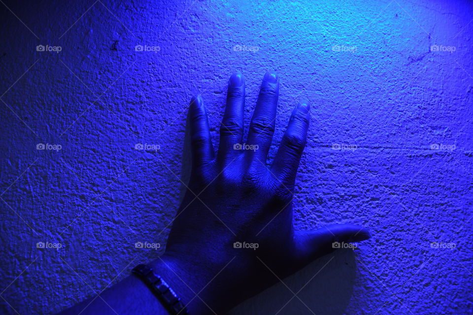 A man places his hand against a stone wall vibrantly lit by fused neon blue lighting.