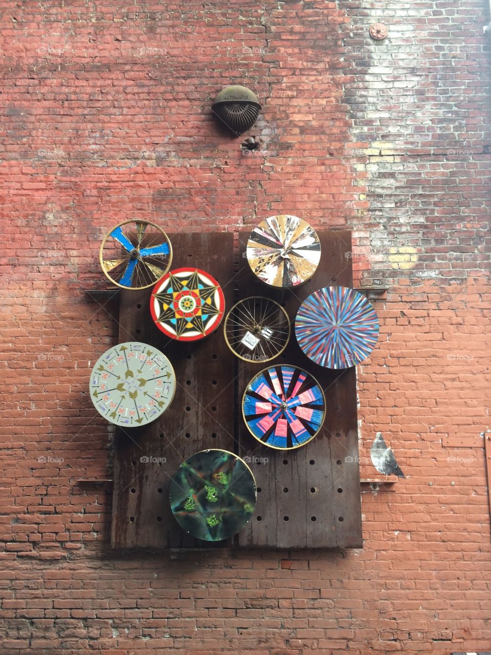 A collection of wind wheels on a piece of wood that's hanging on a city wall in an alley in Seattle.