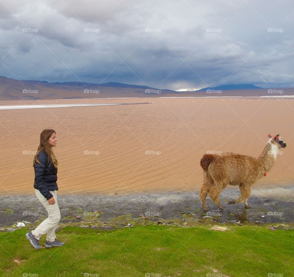Young woman at lake side walking with llama