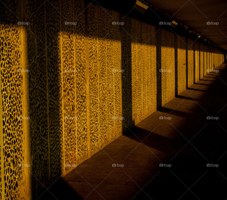 Long shadows are cast along an underground walkway, the walls a decorated with coloured glass