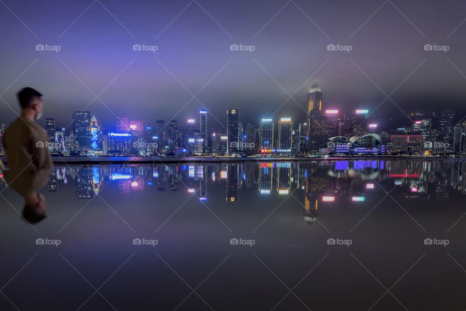 Hong Kong skyline reflected on the Victoria harbor waterfront promenade in Tsim Sha Tsui on a rainy night