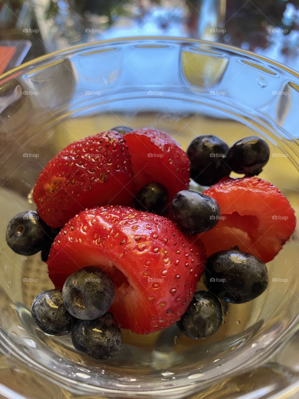 Strawberries red and blueberries blue in a transparent glass bowl for breakfast. Fruits.