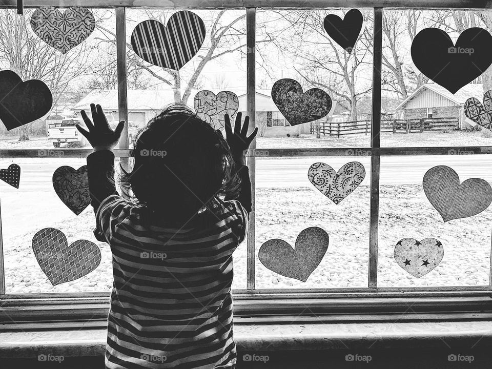 Child admiring hearts on window, toddler celebrating love, toddler looking out window, toddler girl reaching for hearts, black and white portrait 