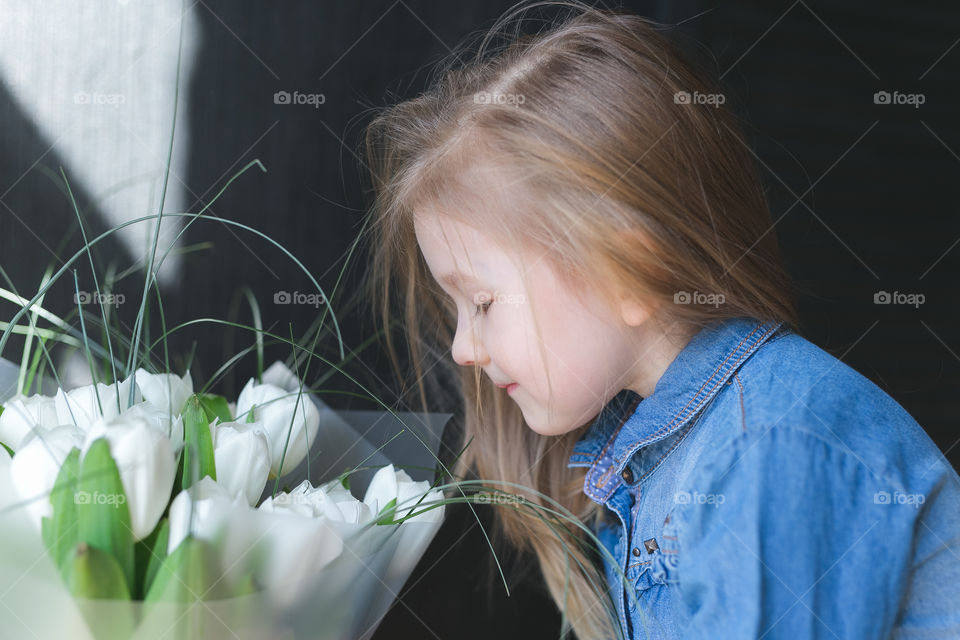 beautiful blonde girl sniffing tulips, the girl is dressed in a denim dress and is at home, black background