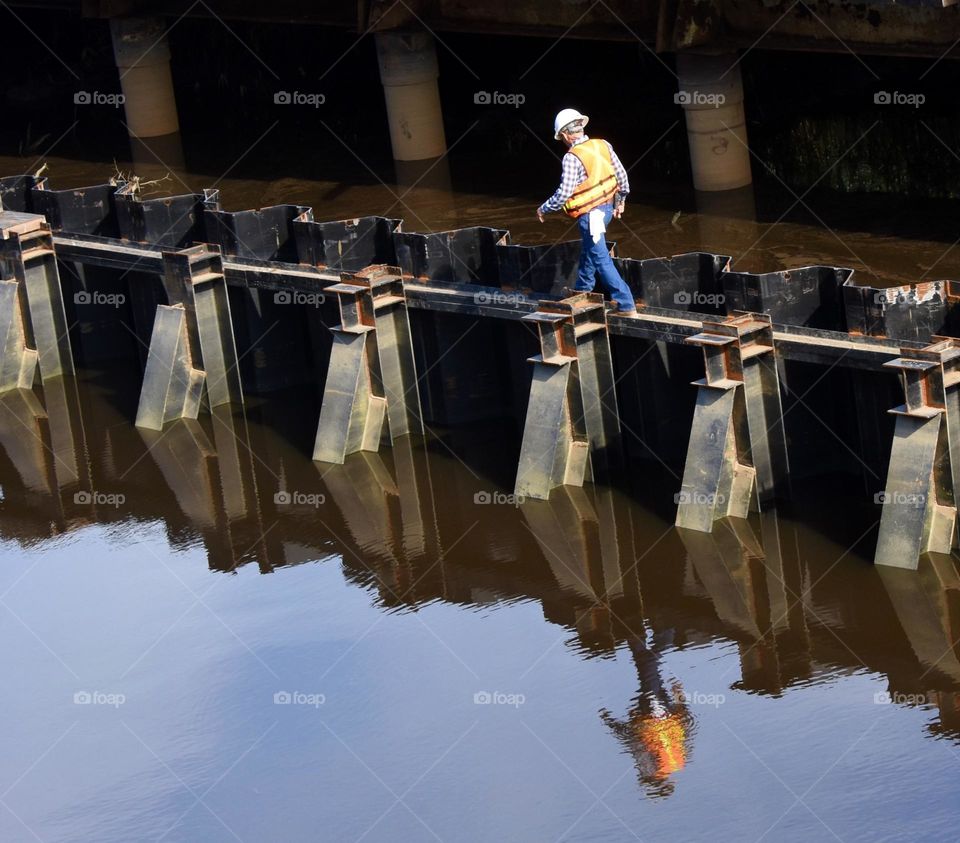 Construction workers walking on beams, reflection in water