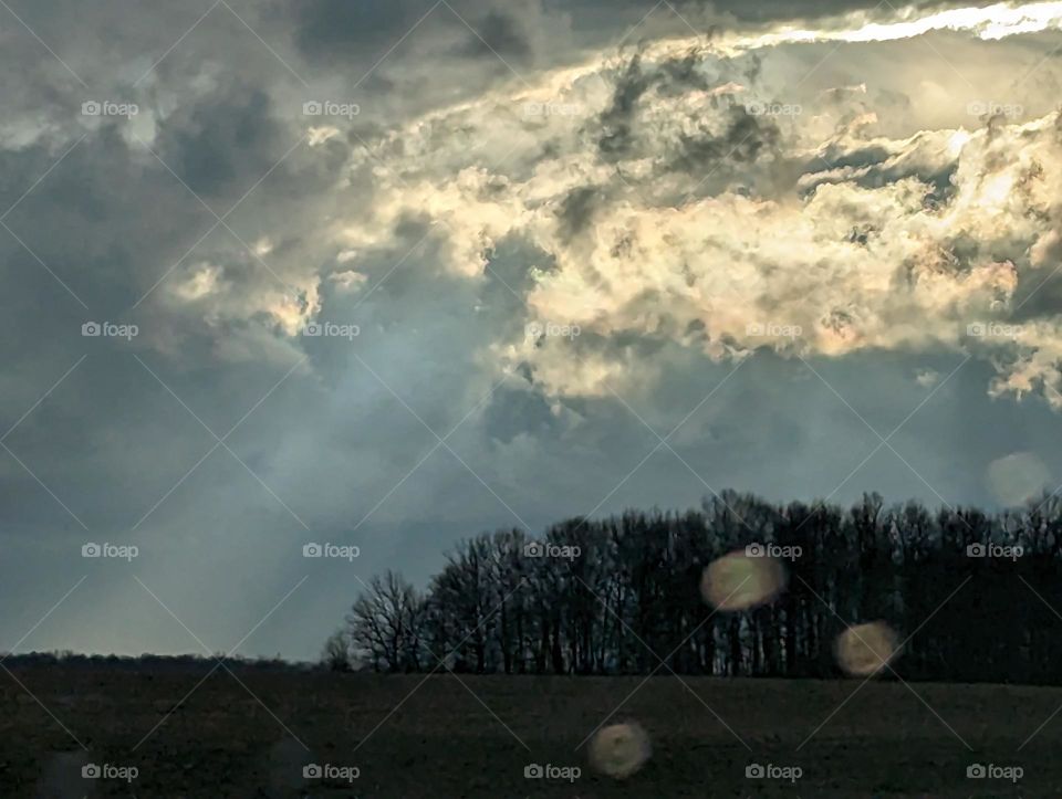 Severe weather clouds over fields and trees through a rainy windshield.