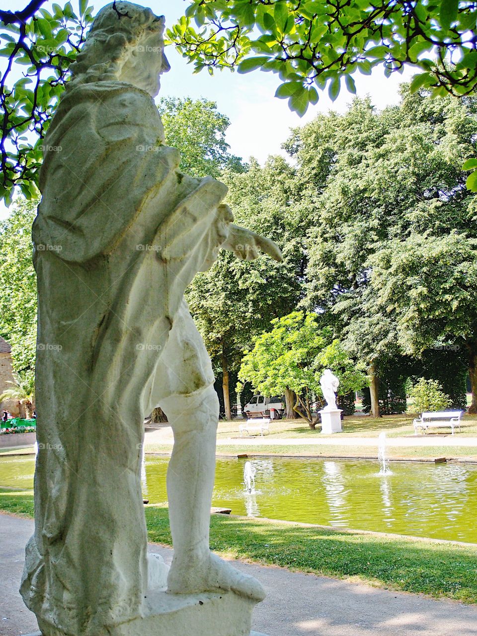 A large statue next to a reflecting pool in an urban park in Europe on a sunny summer day. 