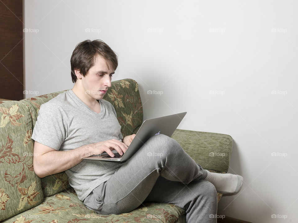 Man seating and working with laptop on sofa at home