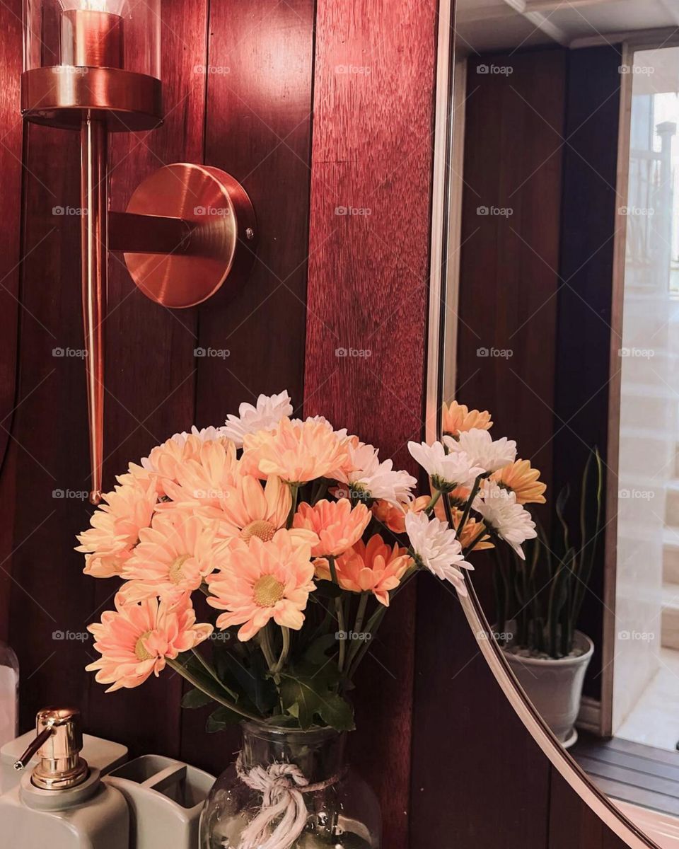 Portrait of a bunch of brightly colored flowers in front of a red wooden door. Bright flowers, including orange and white ones, are placed in a transparent glass vase