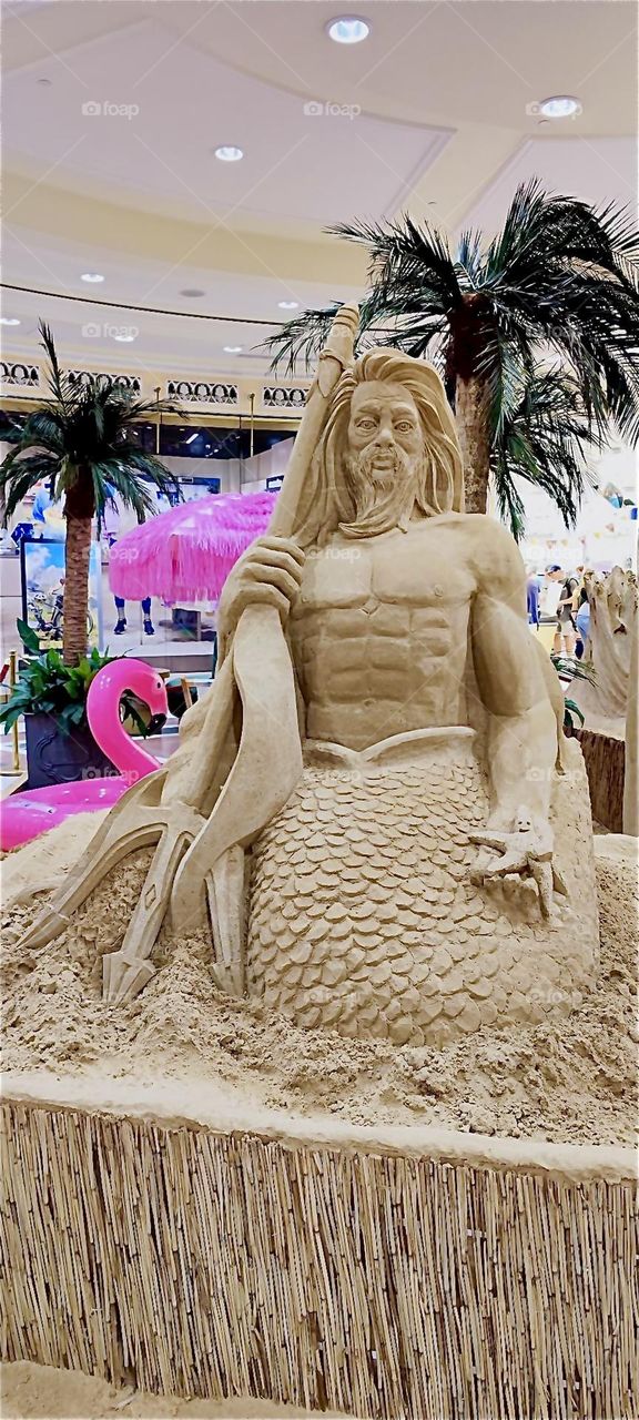 An oversized “Neptune” merman sand sculpture is on display at “das Schloss” or “the Castle”, a large multistory shopping mall in “Berlin”, Germany in the “Steglitz” neighborhood. 2024. Hypnotic Productions