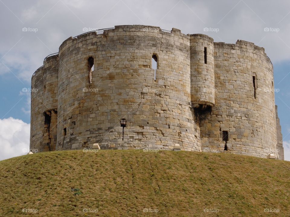 Clifford’s Tower, a local stone landmark in York in England, sits majestically on top of a hill on a sunny day. 
