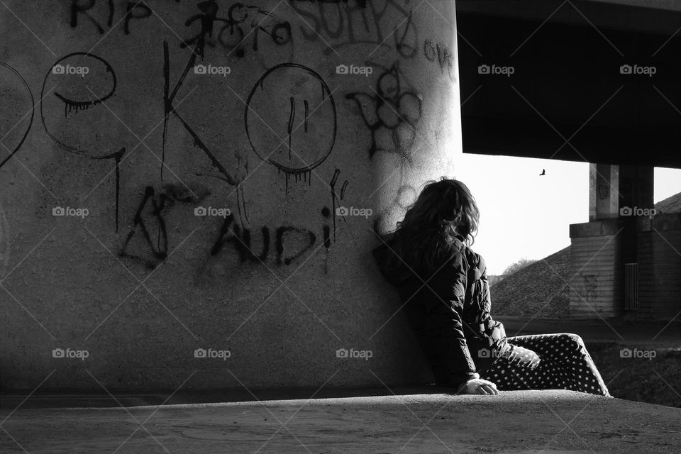 black and white portrait with a woman looking away leaning against a large concrete wall