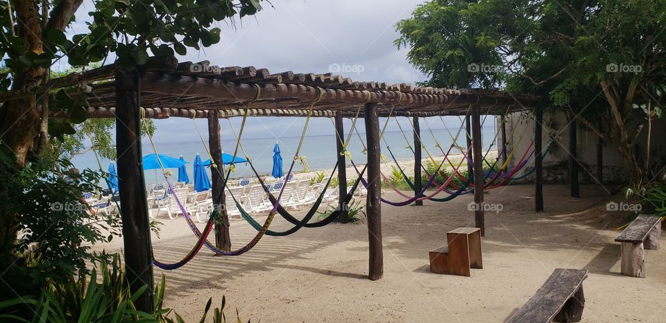 sandy beach with colorful hammocks under a wooden canopy and beach umbrellas.