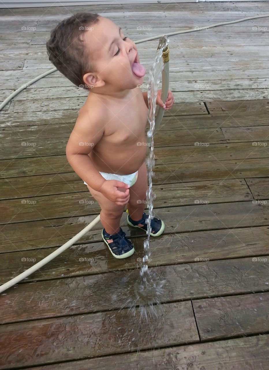 toddler drinking from garden hose. toddler wants a cool drink