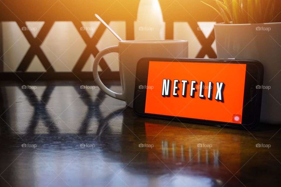 Kuala Lumpur, Malaysia - June 16, 2018:  Smartphone displaying word Netflix on wooden table with selective focus and crop fragment