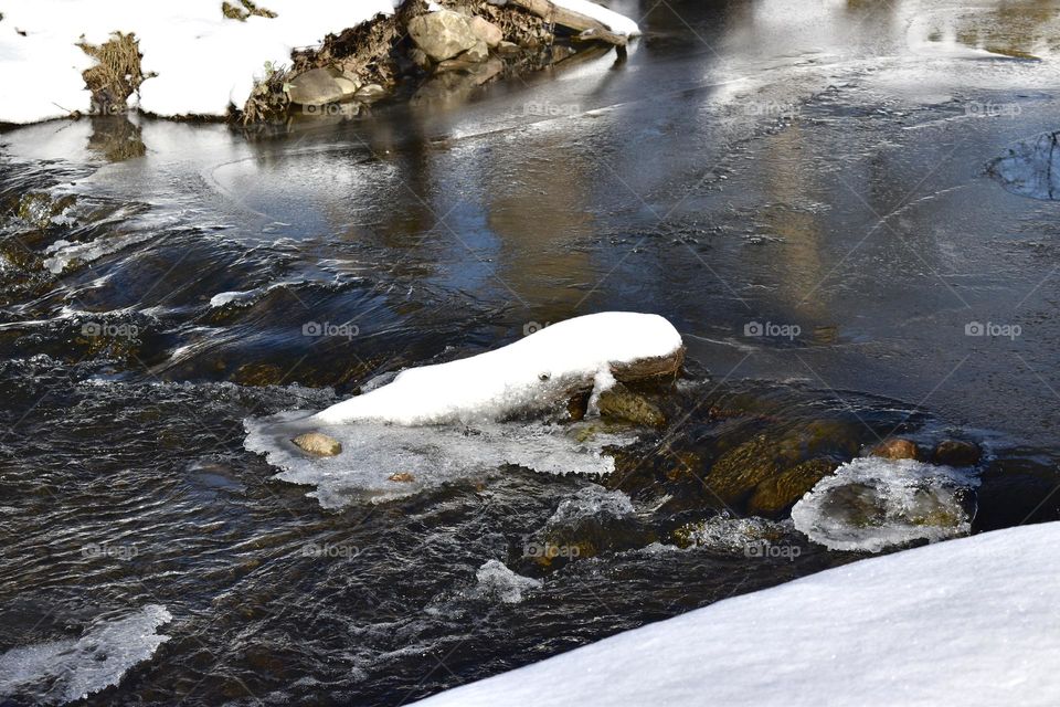 A snow covered log in an icy stream