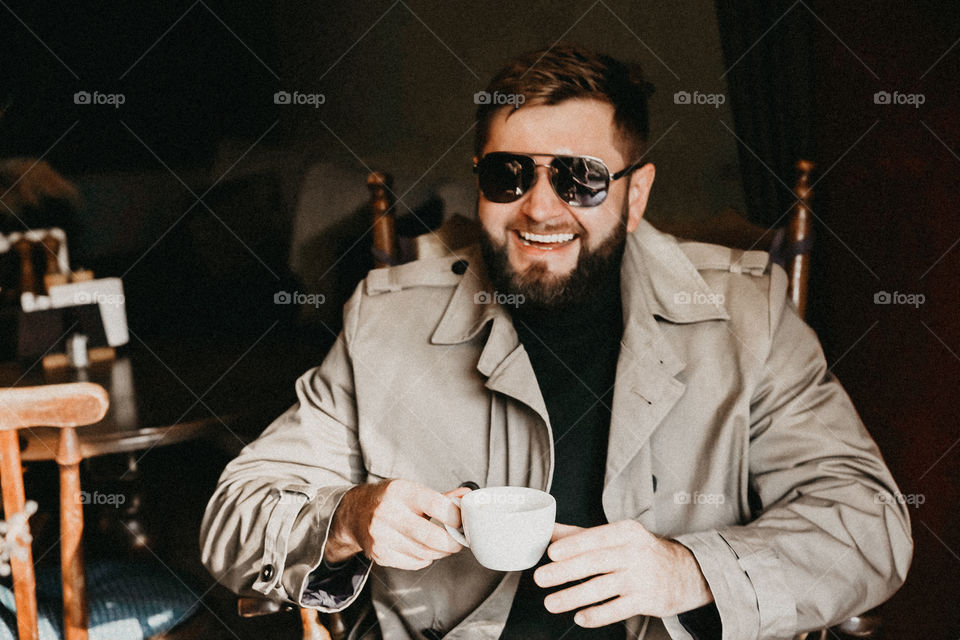 Man in sunglass in brown coat take a cup of coffee and smile