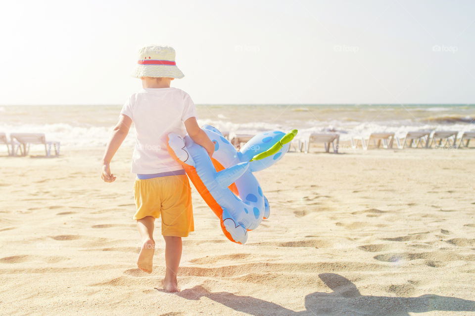 Happy kid with an inflatable circle running along the beach to the sea