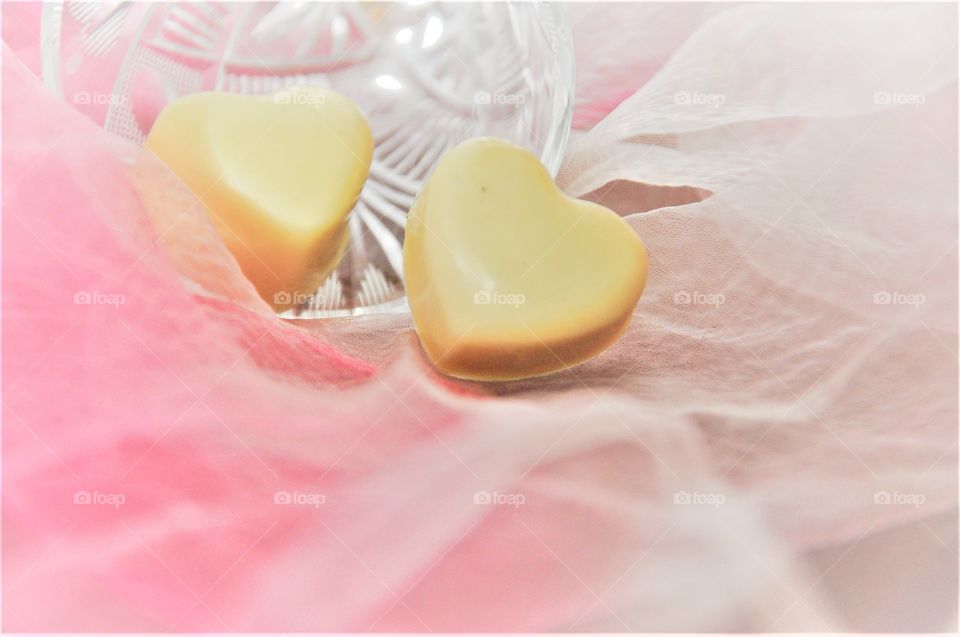 valentine two white chocolate heart shaped sweets in crystal glass and pink background