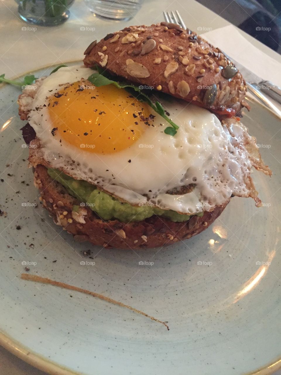An egg on a whole wheat bun with avocado, sausage, and chives 