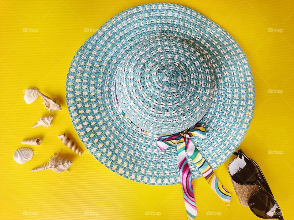 A summer hat and sunglasses on yellow background.