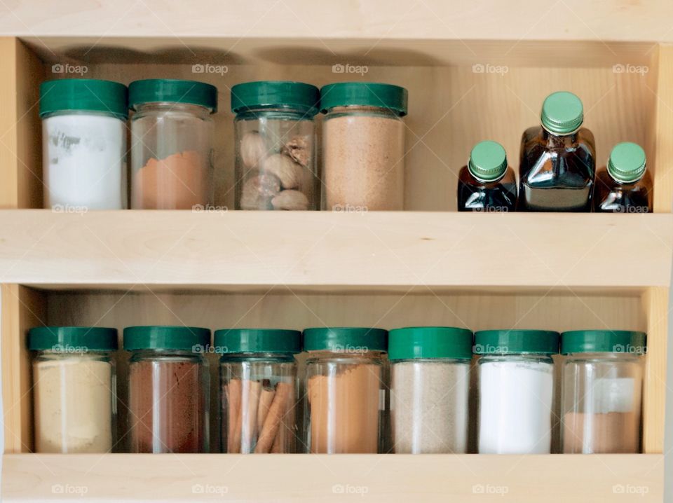 Spices and flavourings with green lids on wooden shelf