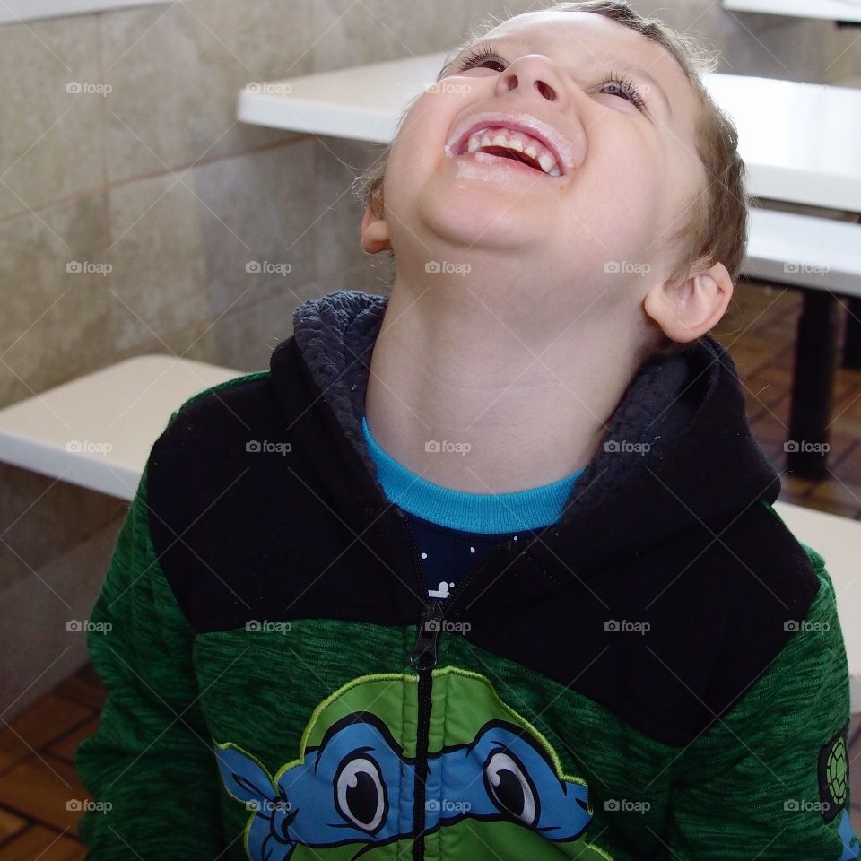 A little boy has a big laugh over the vanilla ice cream covering his mouth after eating a cone for dessert. 