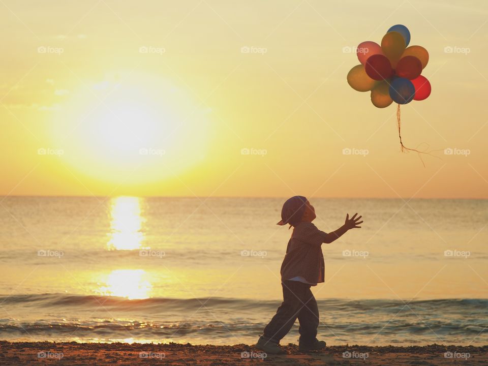 Little boy blowing balloons at beach during sunset