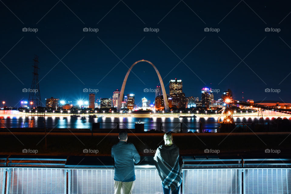 Couple of young adults standing at viewpoint and looking to Gateway arch in St. Louis city in Missouri state , USA at night