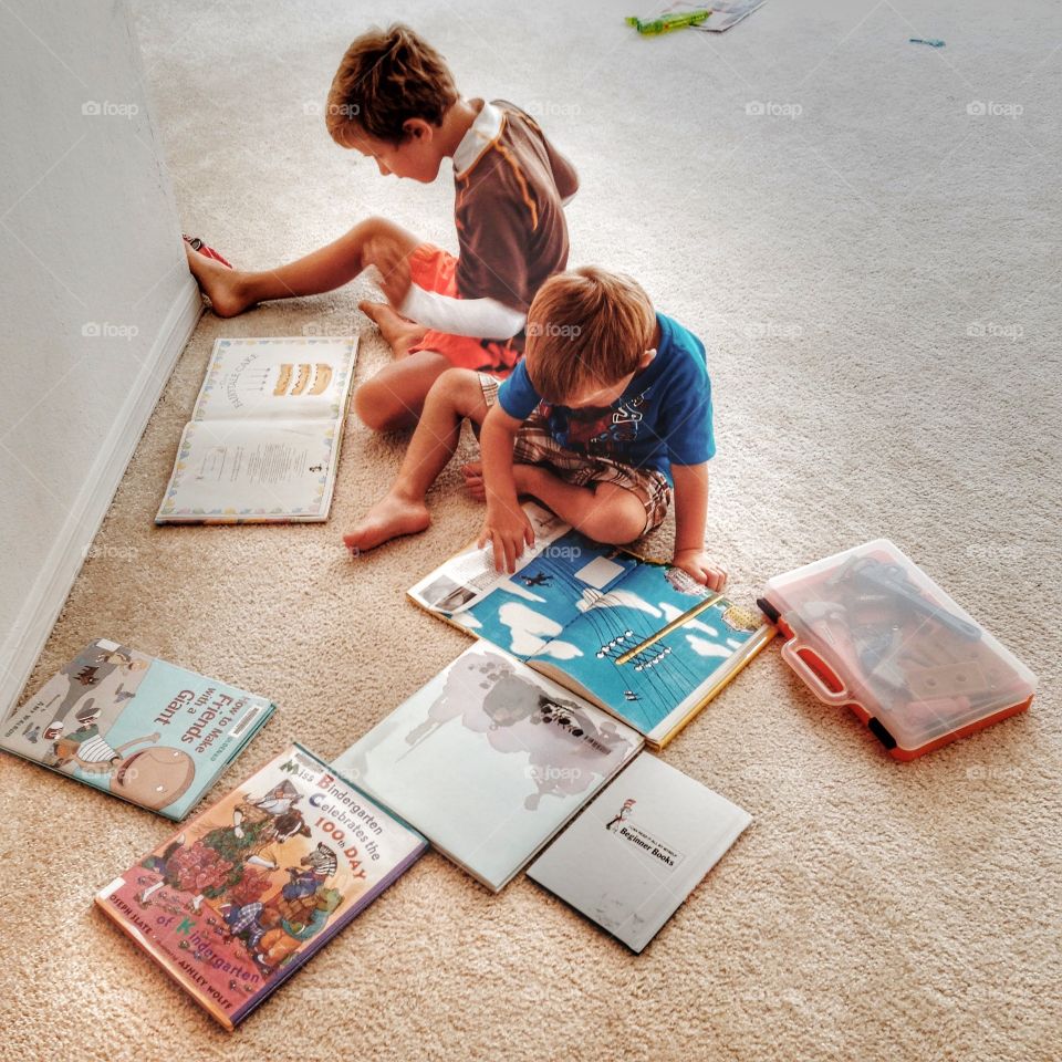 Boys reading books together. The books are scattered on the floor. The boys are very focused on their reading