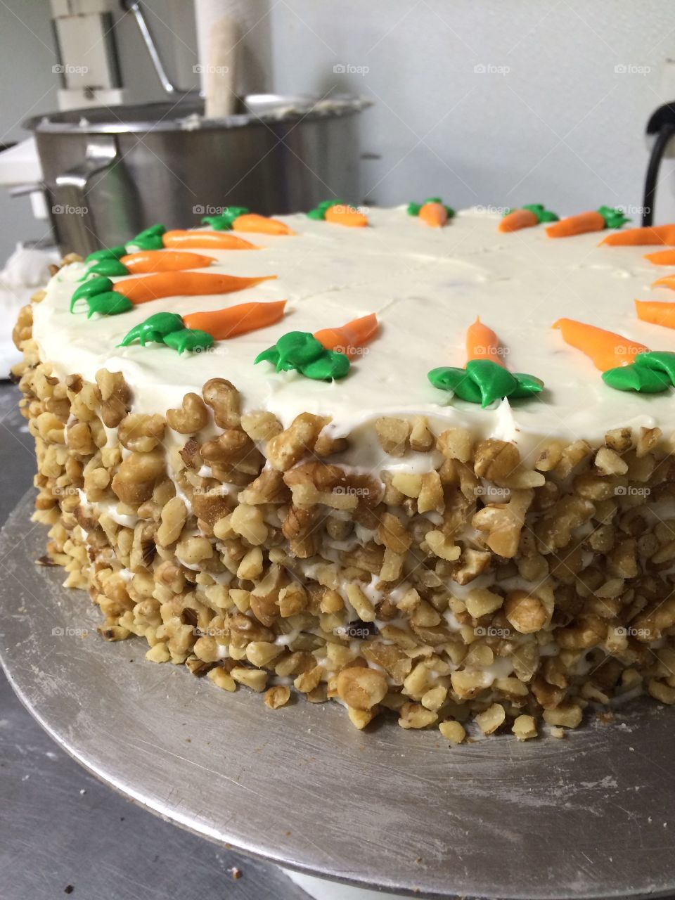 Carrot cake with cream cheese frosting, coated in crushed walnuts and decorated with frosting carrots