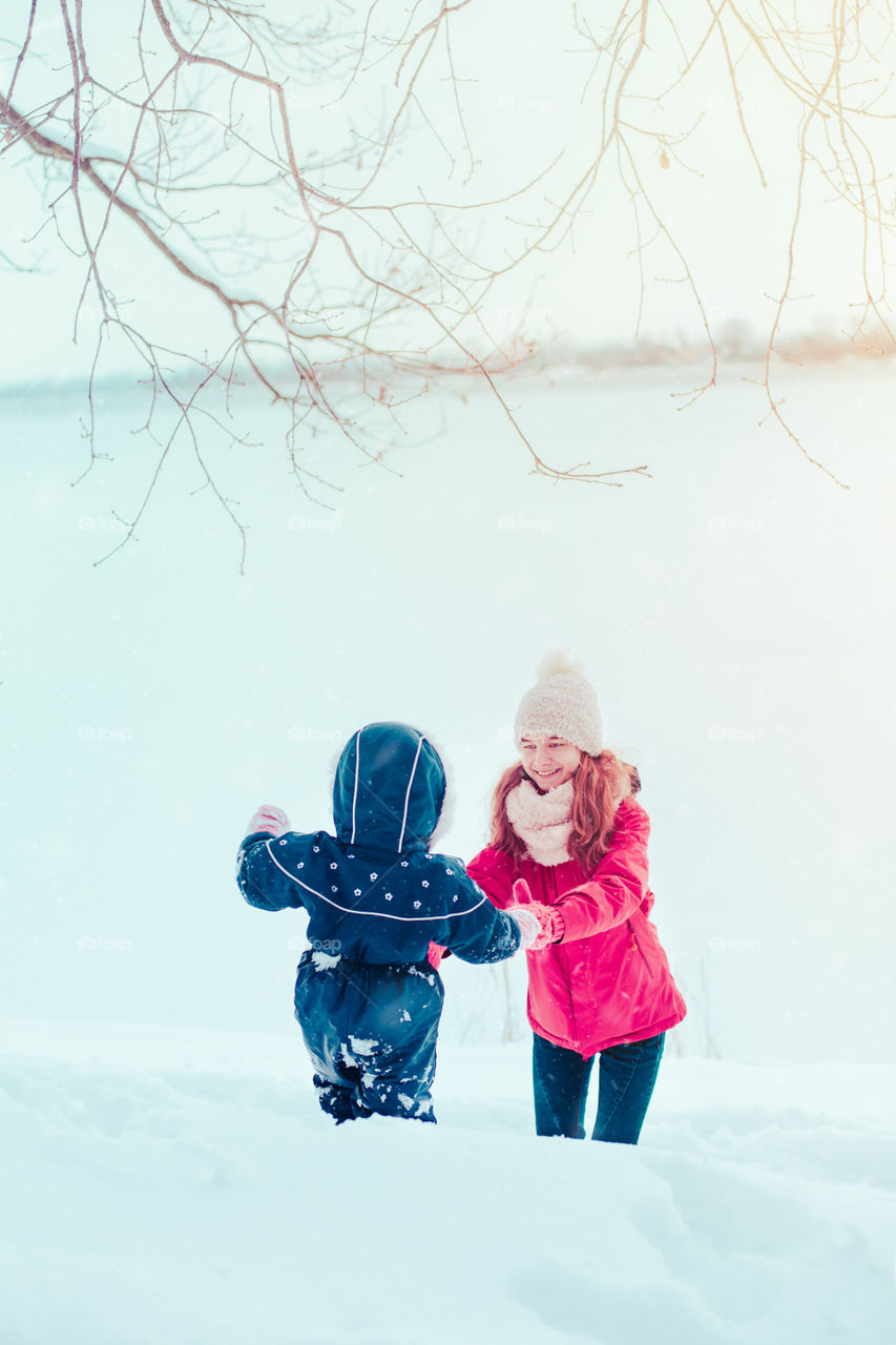 Teenage girl enjoying snow with her little sister. A few years old girl  is walking through deep snow while snow falling, enjoying wintertime. Children spending time together. Girls are wearing winter clothes