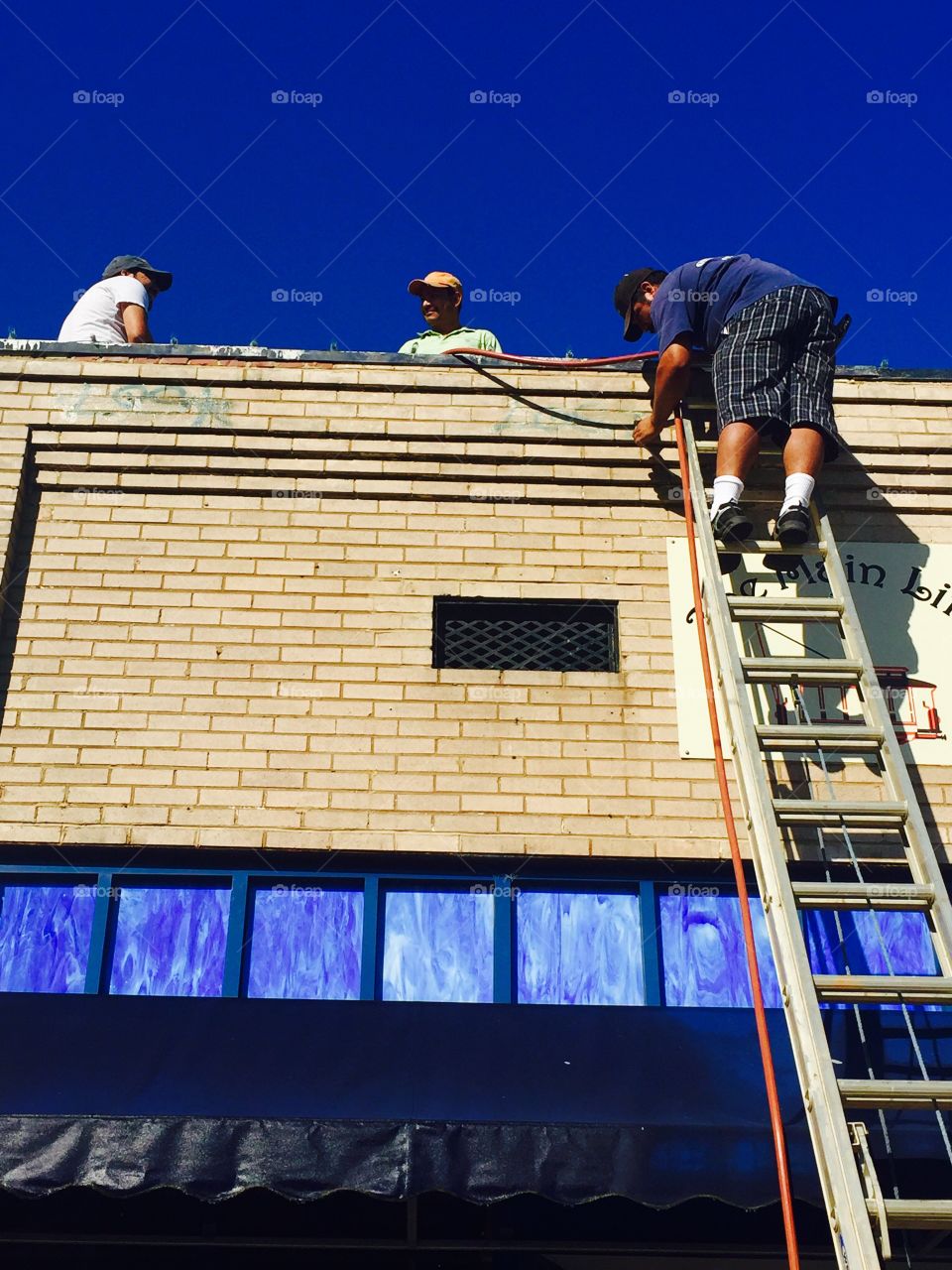 Painters working on painting the front of a small business on a blue sky day