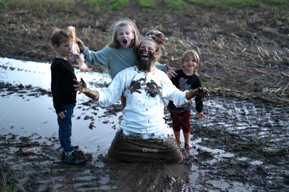 Happy mom with three children having fun on muddy field during autumn