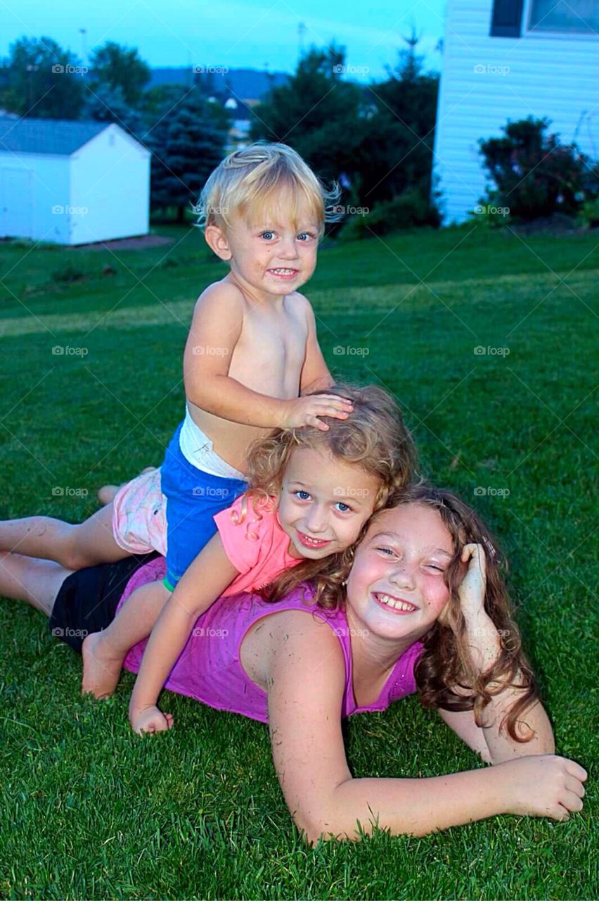 Brother and sisters playing on grass in a heap