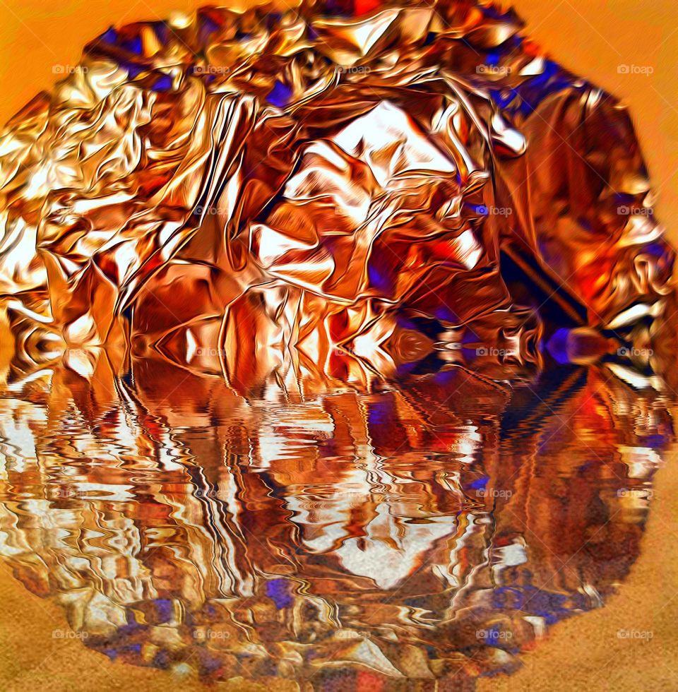 Crumpled ball of aluminum foil under orange light, reflected in water!