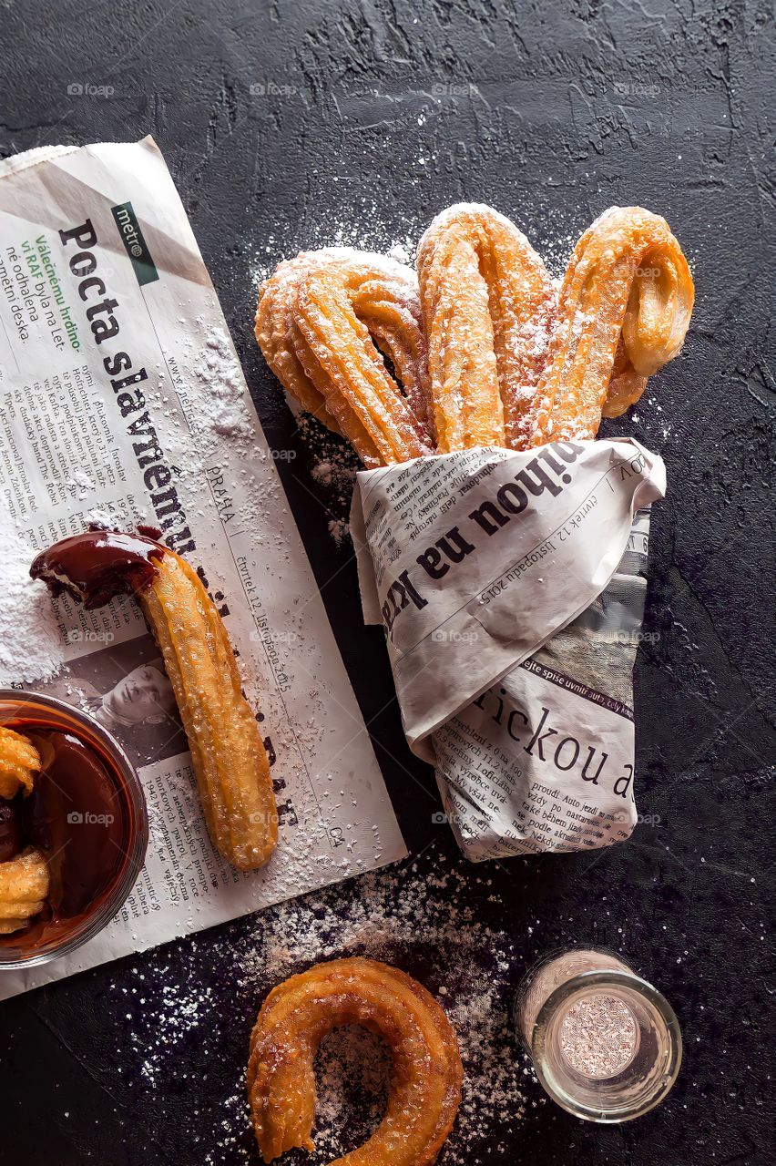 Freshly Baked Churros with glass of chocolate
Churros rolled up in newspaper with melted chocolate dip and powder sugar.