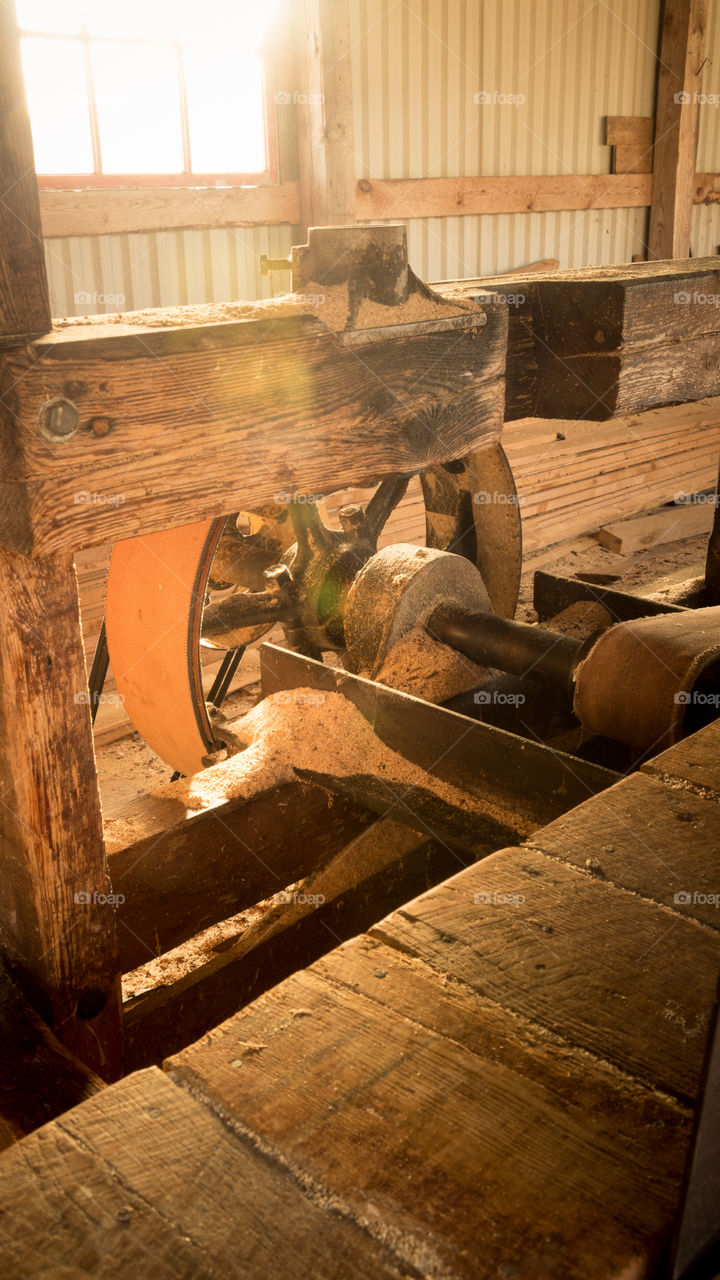 the belt wheel and Axel of a 100 year old sawmill backlit nicely by the sun shining through a small window behind the saw
