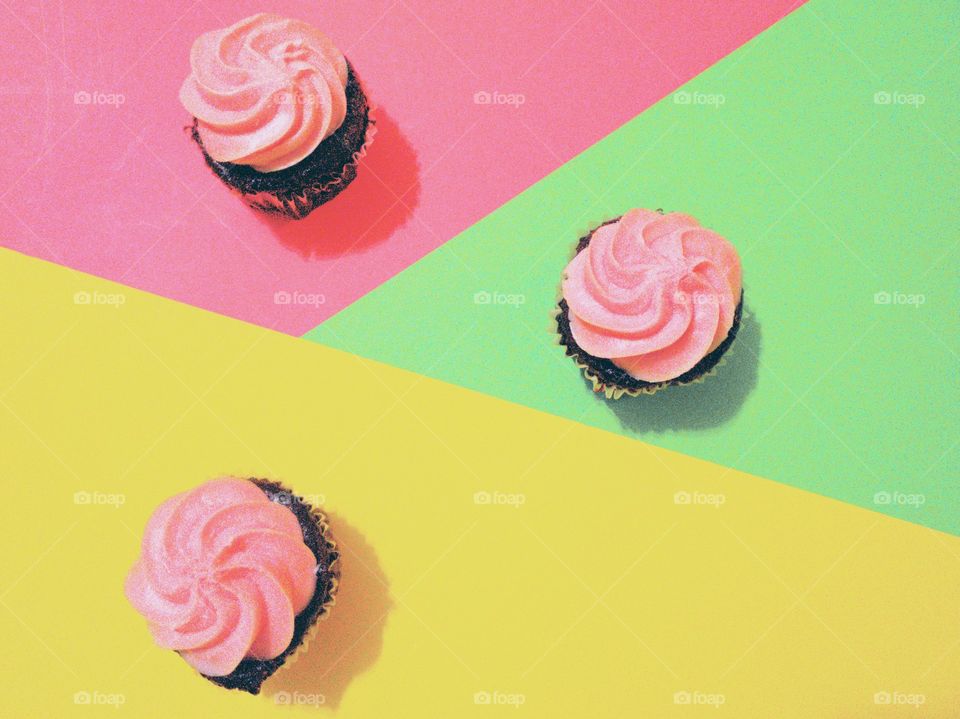 Minimalist photo:  Colorful pastel background and three chocolate cupcakes with pastel pink frosting.