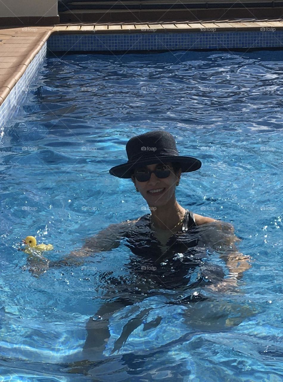 Natural smiling woman protecting from sunshine in pool