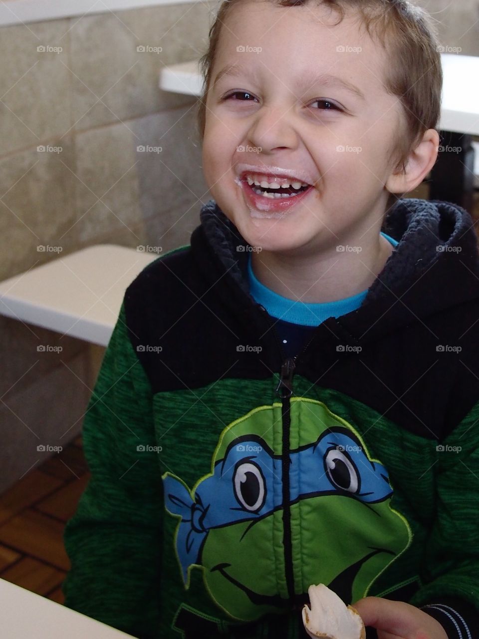 A little boy has a big laugh over the vanilla ice cream covering his mouth after eating a cone for dessert. 