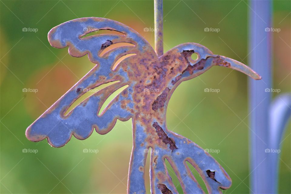 Purple blue Rusty Bird garden ornament against a yellow green blurry background 