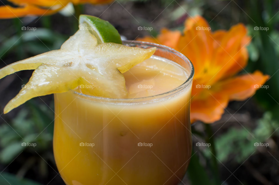 Closeup of fresh yellow and white smoothie garnished with carambola star fruit and slice of lime in garden conceptual healthy lifestyle smoothie blended drinks photography 