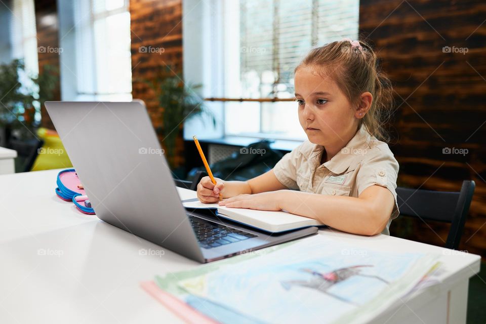 Engaged absorbed student doing her homework using laptop in after school club at primary school. Back to school. Child using technology on elementary computer science class. Smart little girl learning from educational application at school