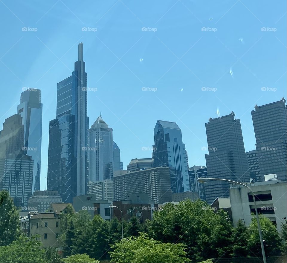 A city skyline against a clear blue sky and trees in the foreground